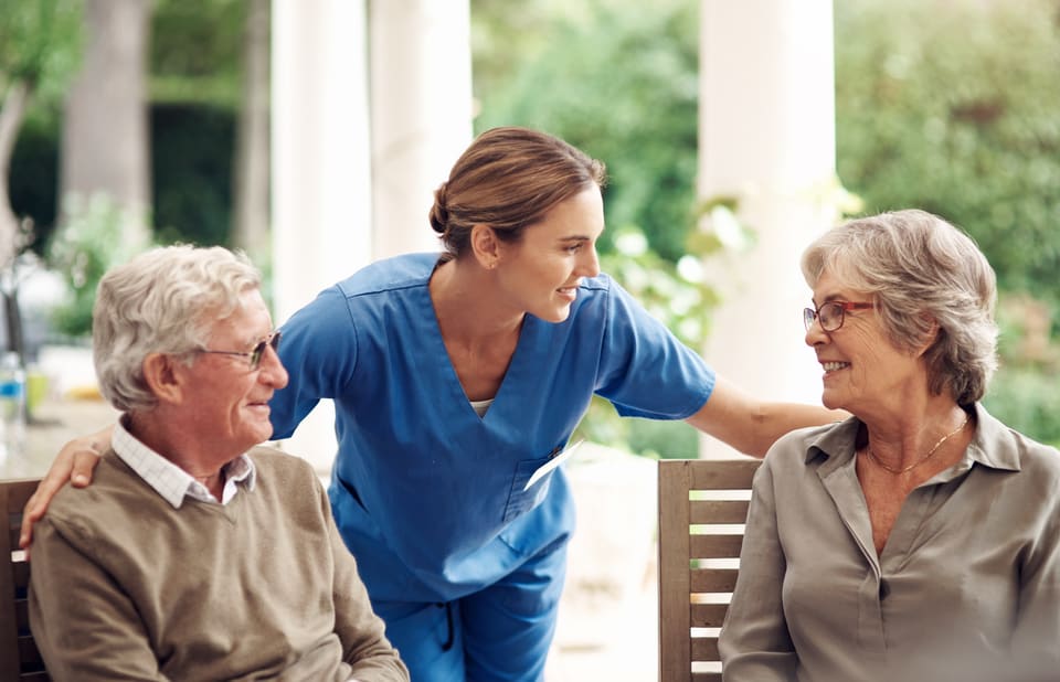 A nurse chatting with an older couple in a sunny garden