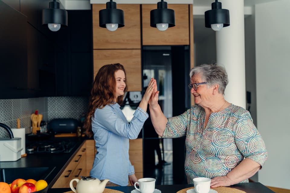 A younger woman and an older woman sharing a high five in a bright kitchen
