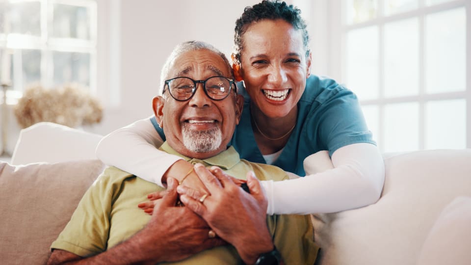 A care worker hugging a laughing older man at home