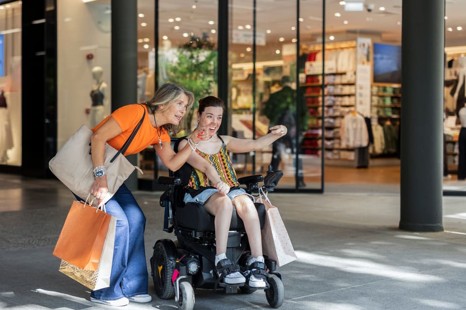 A young woman in a wheelchair out shopping with a friend, both smiling