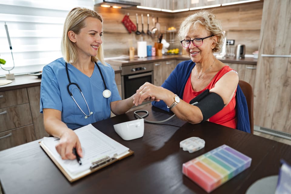 A nurse checking an older woman's blood pressure at her kitchen table