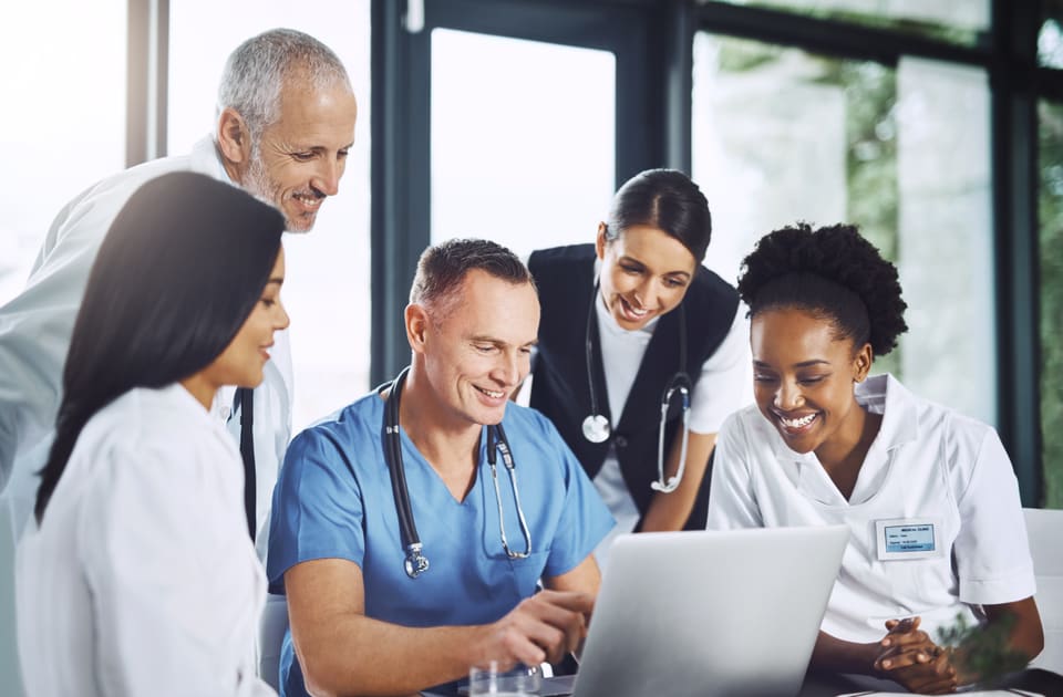 Five clinicians gathered around one laptop, smiling at what is on the screen