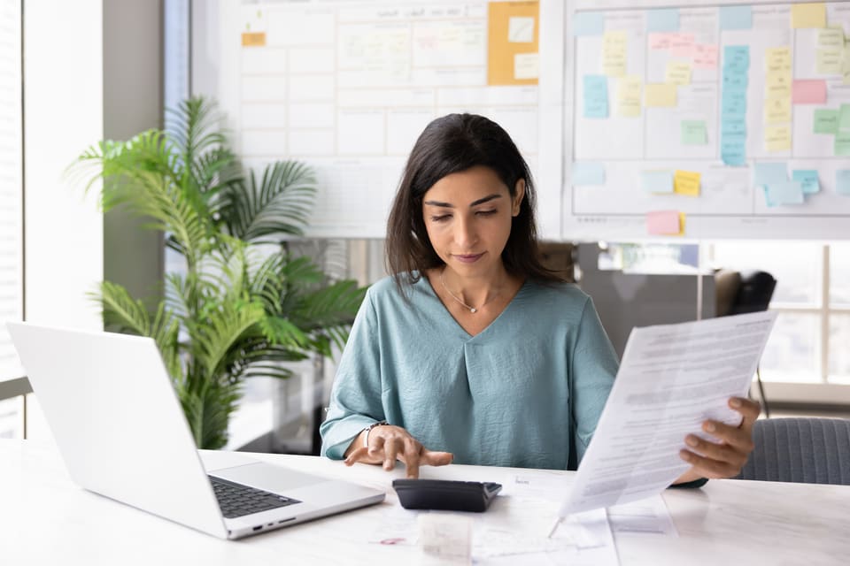 A woman working through figures at her desk beside a wall planner