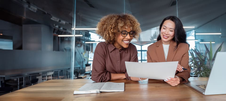 Two women at an office desk reading a printed page together