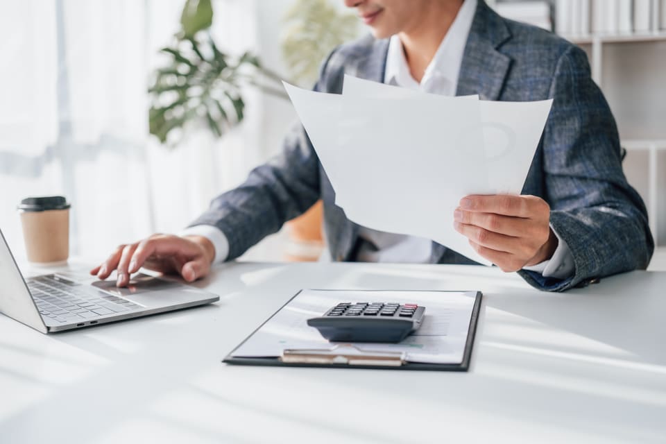 A man reading a printed invoice beside a calculator