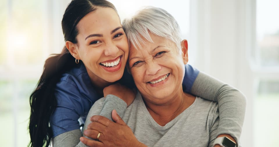 A care worker and an older woman smiling cheek to cheek