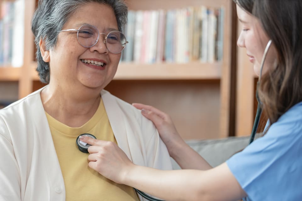 A nurse listening to an older woman's chest with a stethoscope