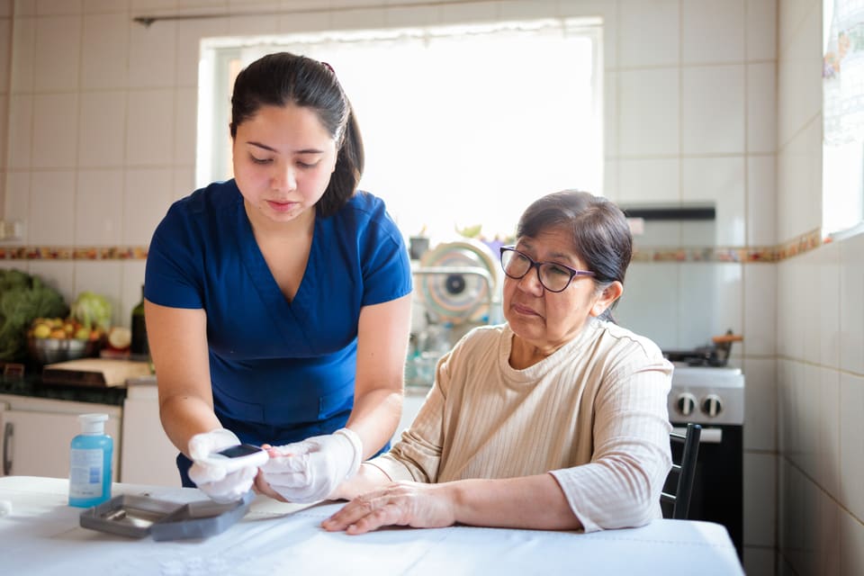 A nurse treating an older woman at her kitchen table