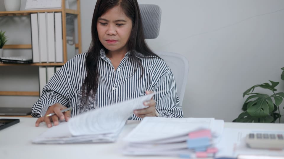 A woman at her desk turning the pages of a thick file