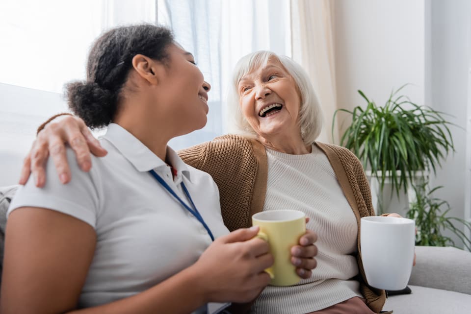 A care worker and an older woman sharing a laugh over tea