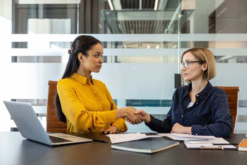 Two women shaking hands across an office desk