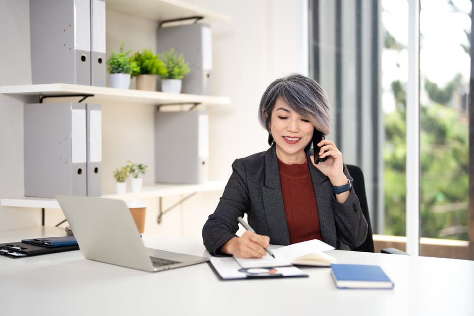 An office manager smiling as she takes a call and notes a change in her planner