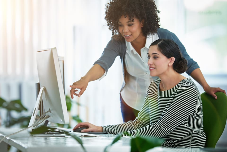 One colleague leaning over another's shoulder to point at her computer screen