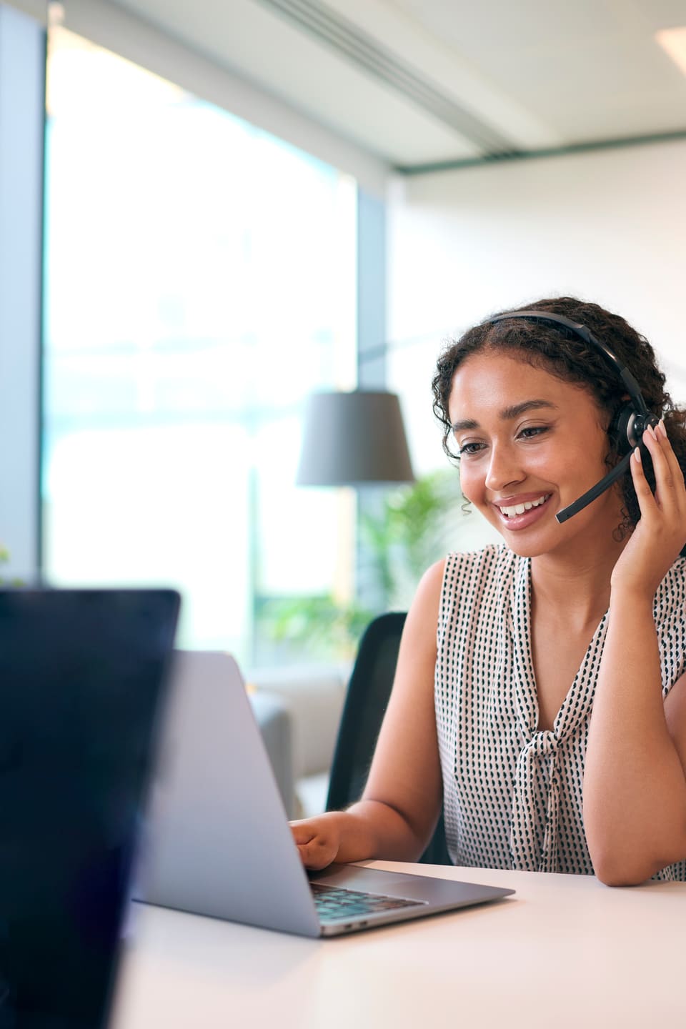 A woman wearing a headset, smiling on a call at her laptop