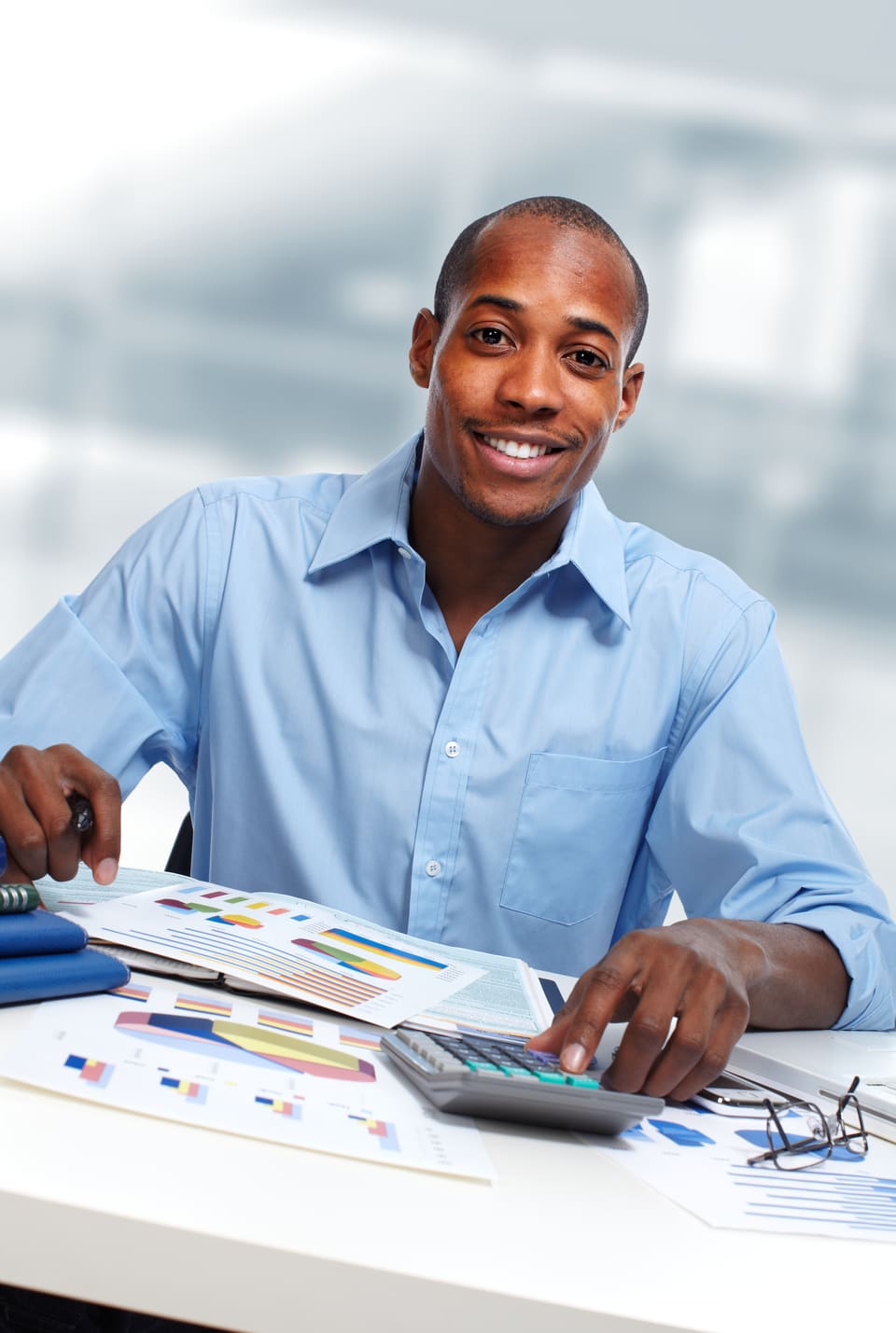 A man in a blue shirt at his desk with a calculator and printed figures