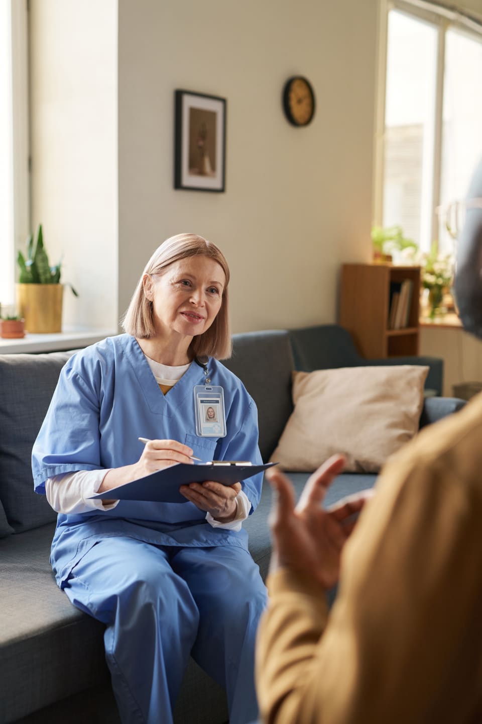 A nurse with a clipboard listening to someone in a lounge room