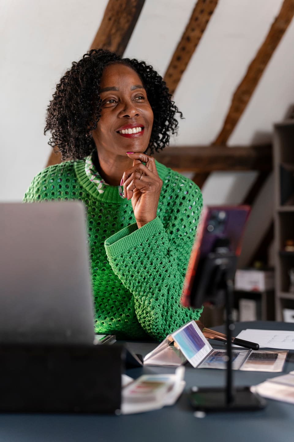 A woman at her laptop looking up and smiling, her hand at her chin