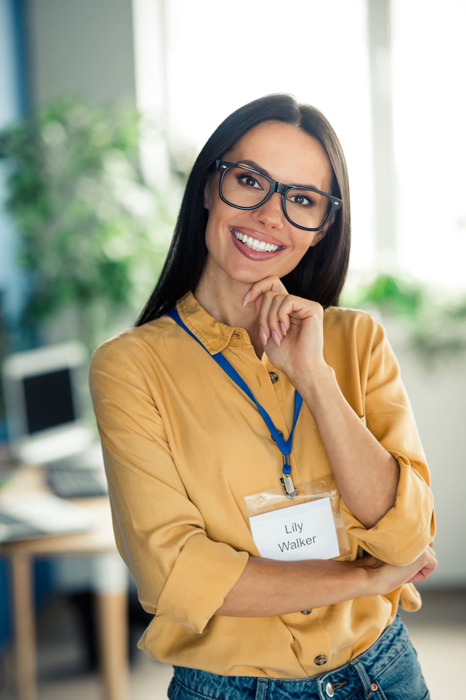 A smiling woman in glasses wearing a lanyard with a name badge