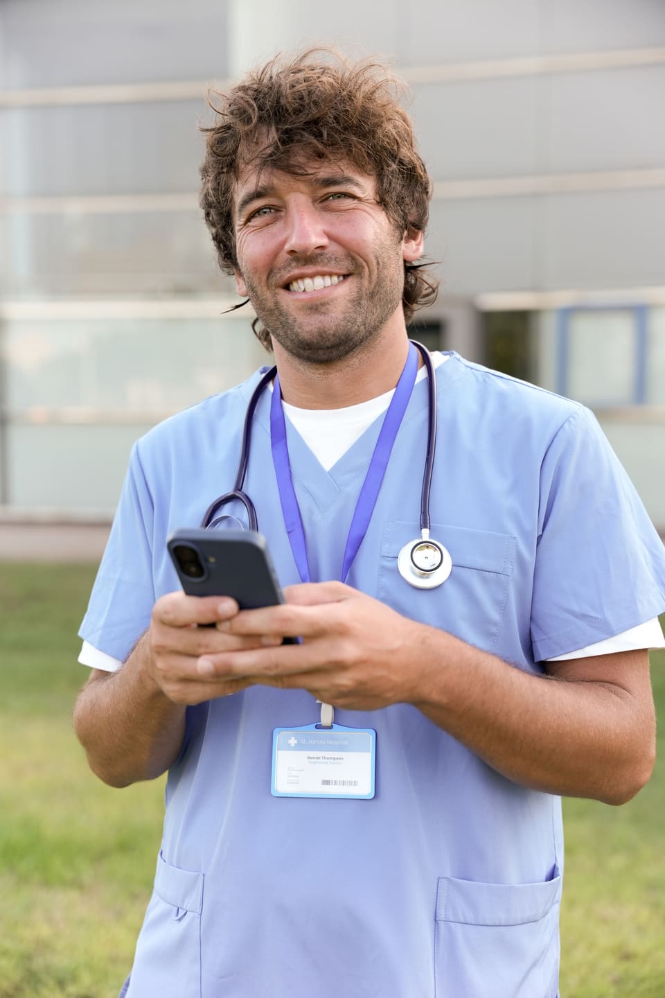 A nurse in scrubs smiling as he checks his phone