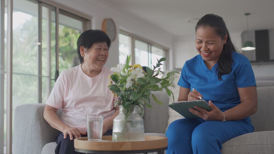 A care worker with a tablet sitting with an older woman