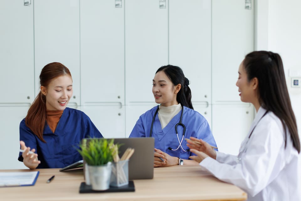 Three colleagues in scrubs talking at a table