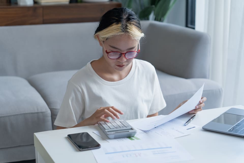 A young woman working through paperwork with a calculator