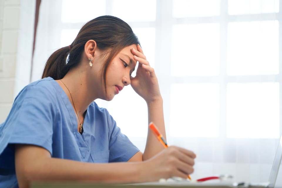 A tired nurse at her desk with her head in her hand