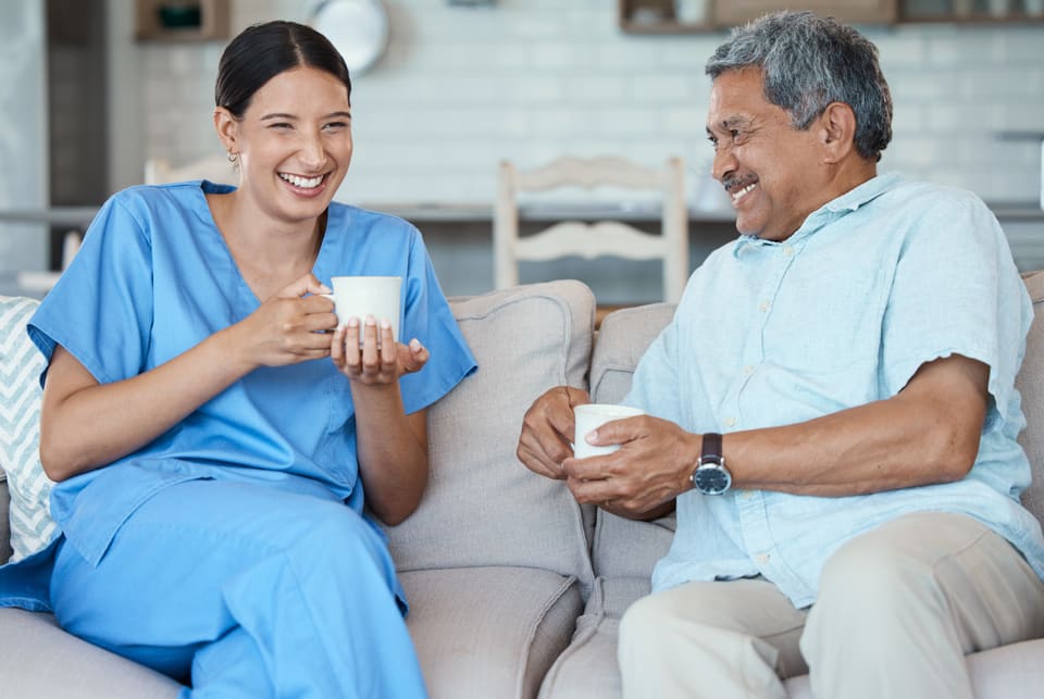 A nurse and an older man laughing over a cup of tea