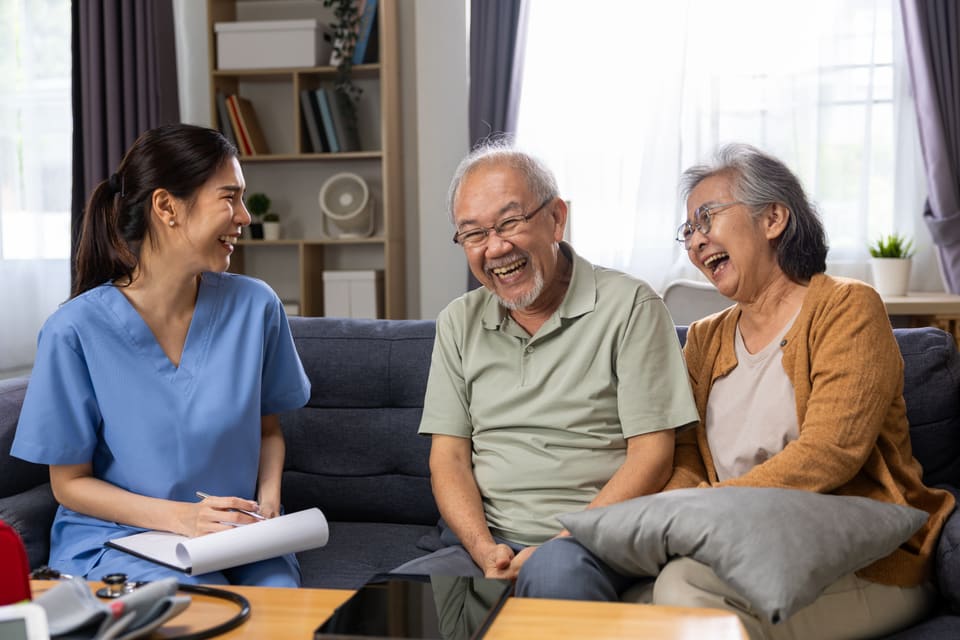A care worker laughing with an older couple on their couch