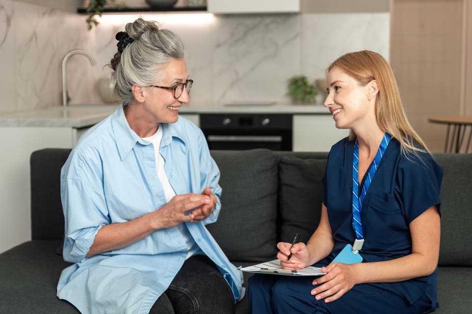 A care worker talking with an older woman on her couch