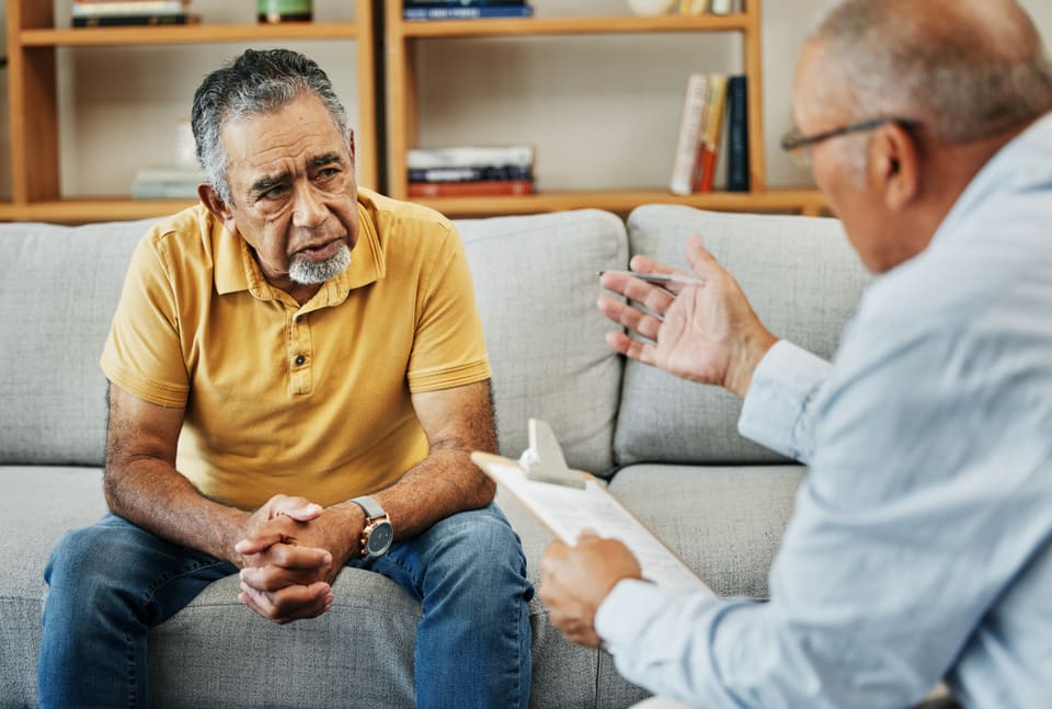 An older man talking with a clinician who is taking notes