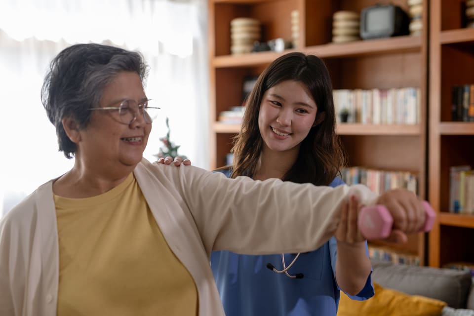A therapist helping a smiling older woman with an arm exercise