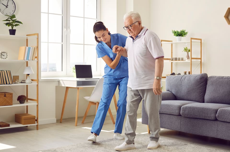 A nurse helping an older man walk across his living room