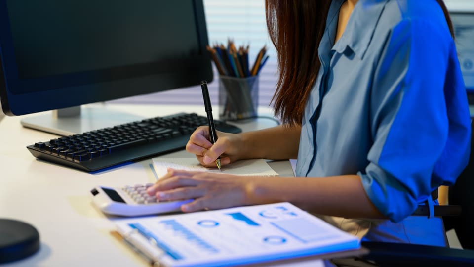 A woman checking figures on her computer against printed papers