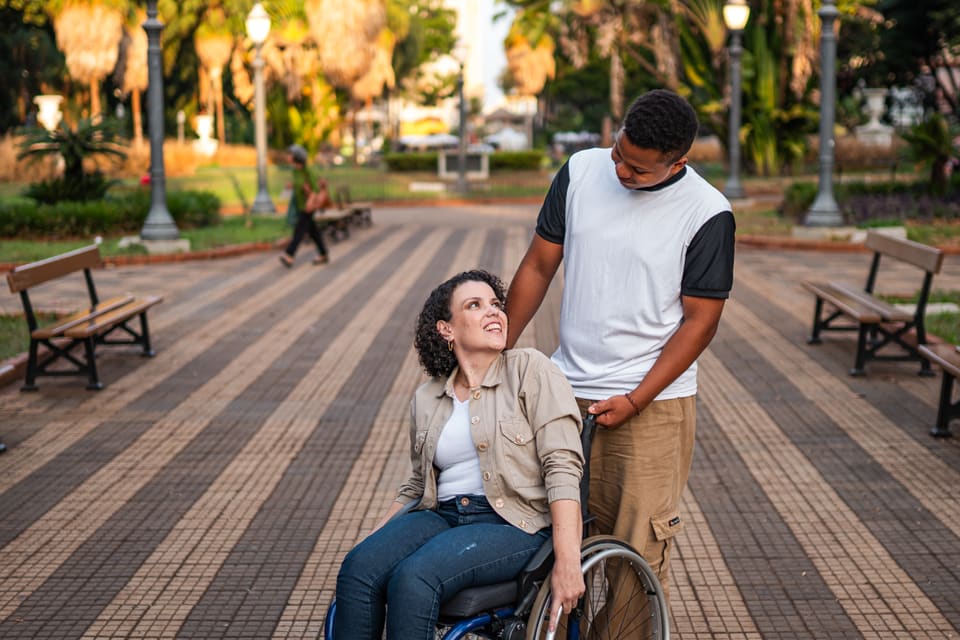 A young woman in a wheelchair laughing with a friend in a park