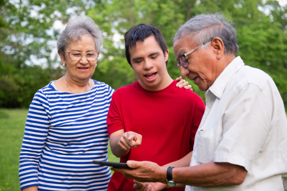 An older couple with their adult son, looking at a phone together