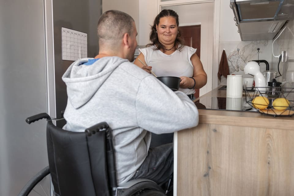 A man in a wheelchair talking with a woman in their kitchen