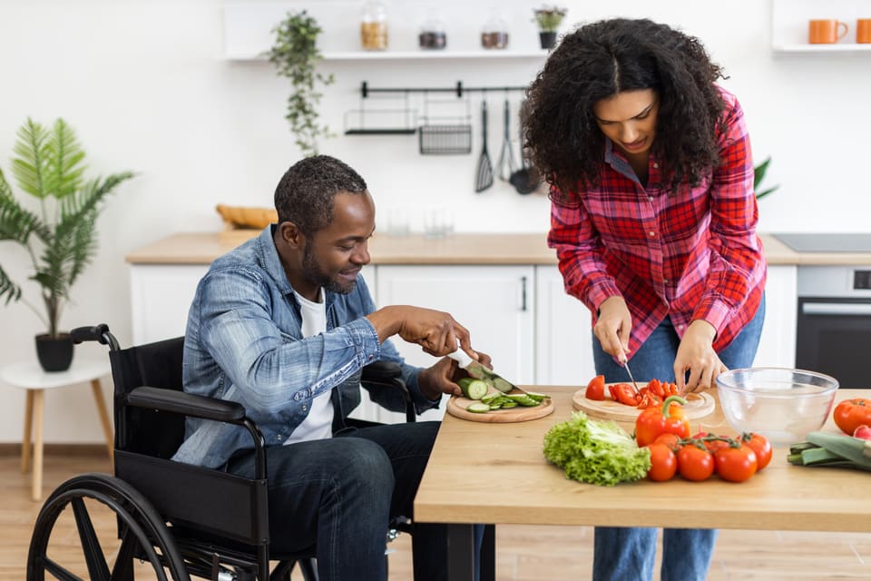 A man in a wheelchair cooking with a support worker
