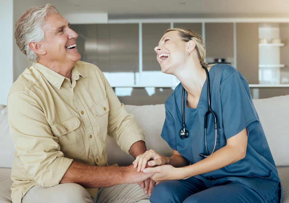 A nurse and an older man laughing together, holding hands
