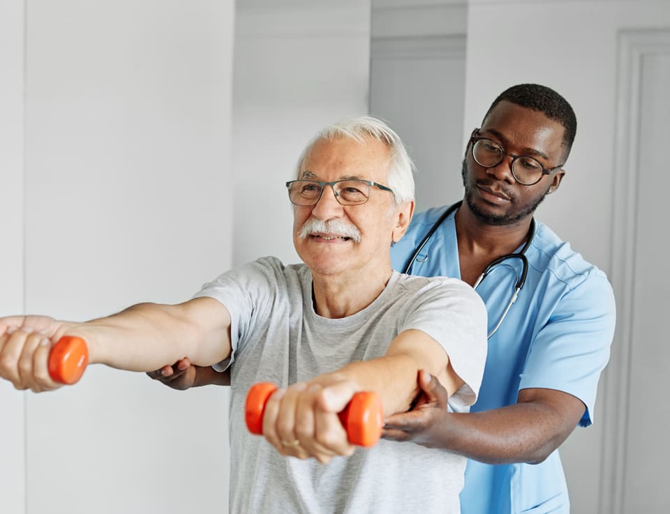 A physiotherapist guiding an older man through a light weights exercise at home