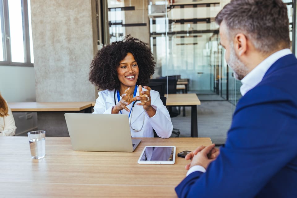 A smiling woman at her laptop talking with a colleague