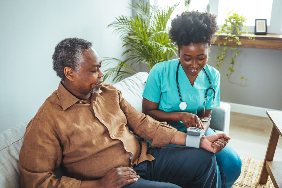 A nurse checking an older man's blood pressure in his living room