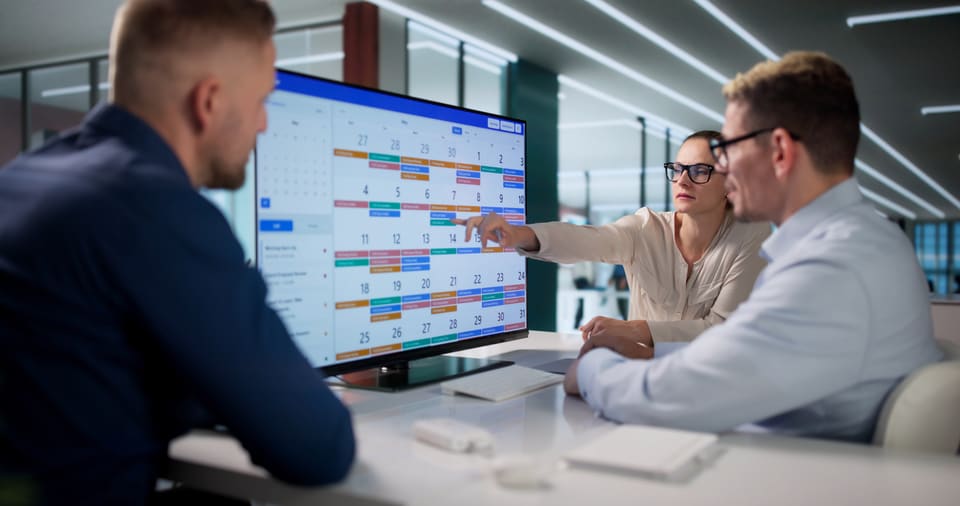 Two colleagues reviewing a weekly schedule on a large office screen