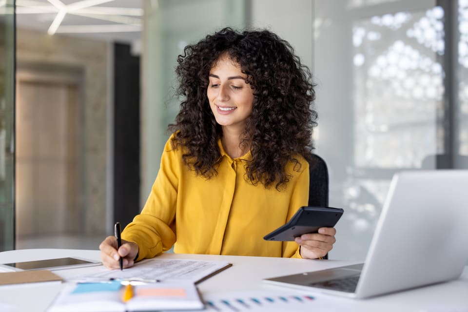 A smiling woman working through figures with a calculator at her desk