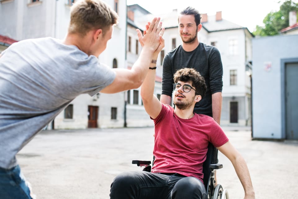 A young man in a wheelchair high-fiving a friend in the street