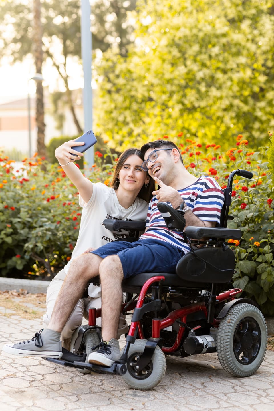A young man in a power wheelchair taking a selfie with a friend outdoors