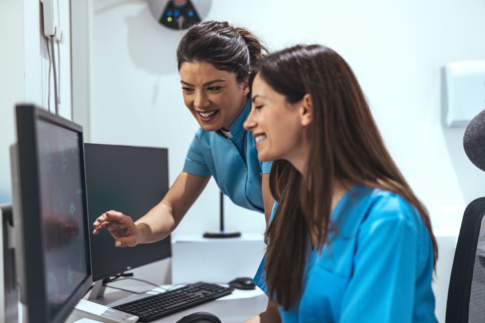 Two nurses smiling as they look through something on a desktop computer together