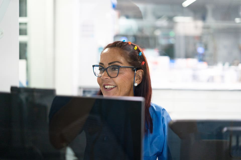 A woman in scrubs smiling at a computer screen in an office