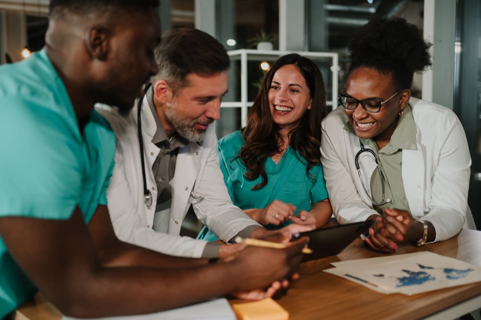 A care team leaning over a table together, laughing as they review papers and a tablet