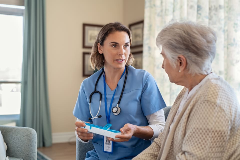A nurse in blue scrubs talking with an older woman at home